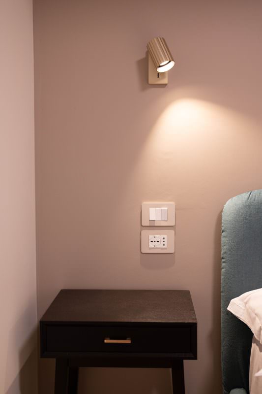 Comodino accanto al letto con applique orientabile e prese di servizio