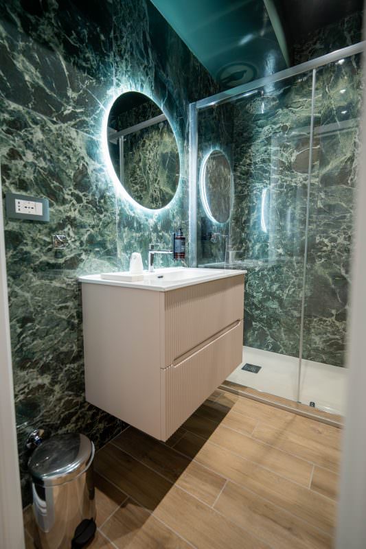 Bagno rivestito in marmo verde con lavabo e specchio retroilluminato
